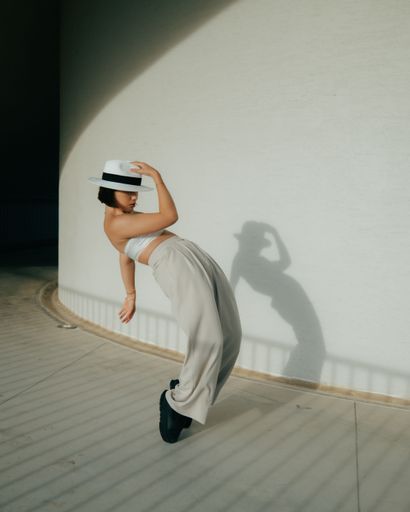 A young woman in stylish attire poses dramatically against a wall, casting a shadow
