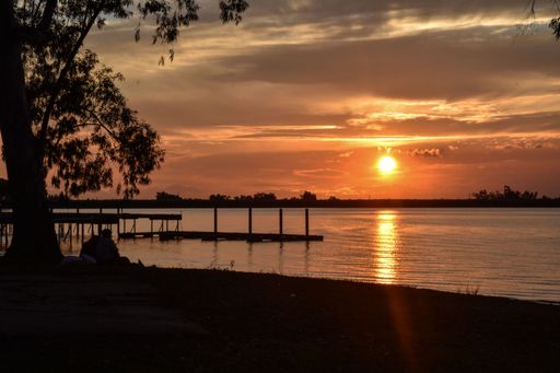 A beautiful sunset over a calm lake with a silhouette of trees and a pier in the foreground