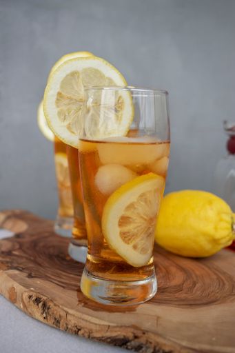 Three glasses of iced tea with lemon slices on a wooden board