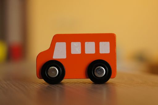 A selective focus shot of an orange wooden toy car on a wooden surface