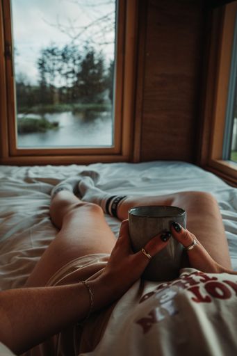 A cozy scene of a person relaxing in bed with a cup of coffee and a view of a lake through the window