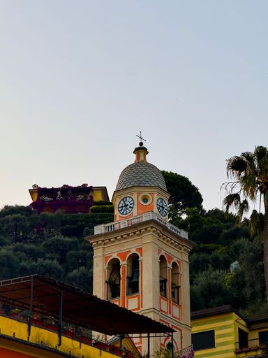 A picturesque clock tower in Portofino, Italy, with a clear sky and surrounding greenery