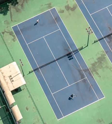 An aerial view of two people playing tennis on  a brightly colored tennis court