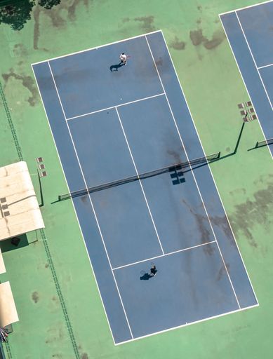 An aerial view of two people playing tennis on  a brightly colored tennis court