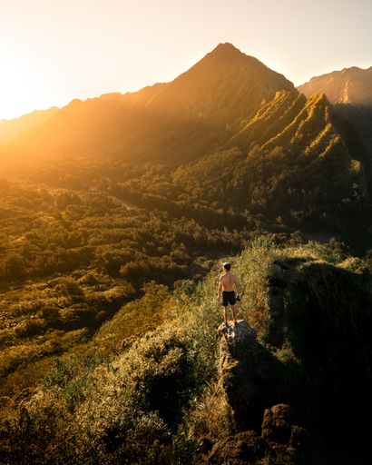 A high angle shot of a male standing on top of a cliff and enjoying the breathtaking view of the mountain during sunrise