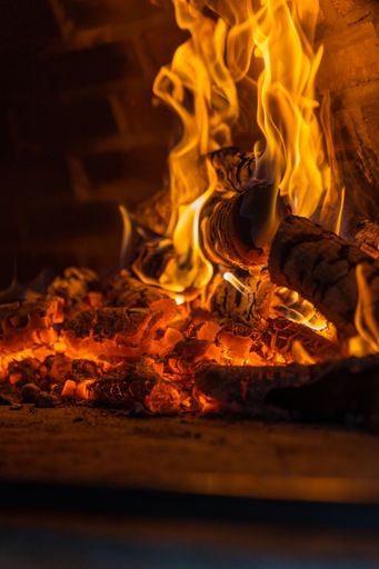 Close-up of burning firewood inside brick oven with bright flames and glowing embers in a fireplace