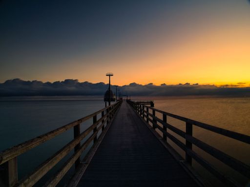 A serene pier extending into the calm sea at sunset with a vibrant sky