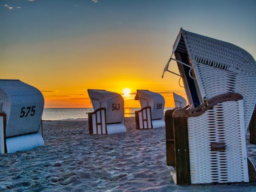 Sunset at a beach with wicker beach chairs on the sand and a calm sea in the background