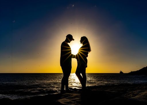 Silhouette of a couple holding hands at sunset on a beach with the sun setting behind them
