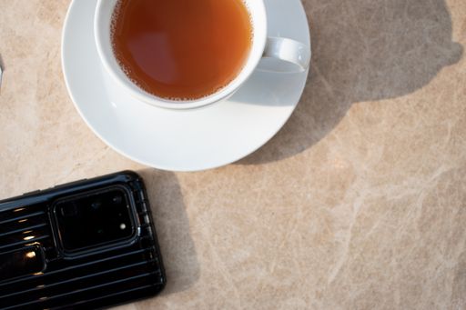 An overhead shot of a cup of hot tea on white saucer beside a mobile phone - office break concept