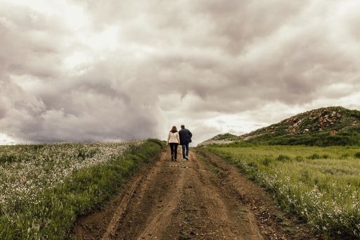 A shot of a male and female walking along a pathway in a valley with flowers under a foggy sky