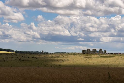 A panoramic view of Stonehenge under a partly cloudy sky, with tourists in the background