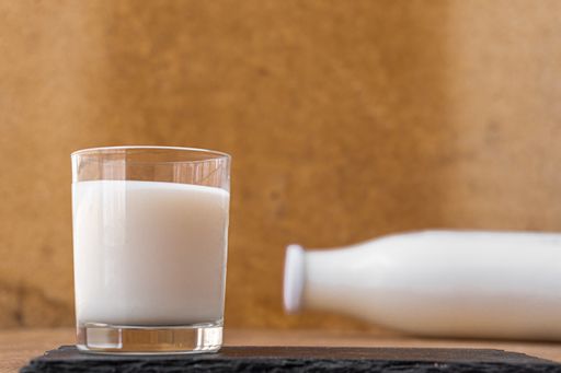 A closeup of a glass of fresh milk and a bottle in the blurry background on the table