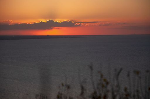 A stunning sunset over a calm sea with a vibrant orange sky and silhouetted clouds.