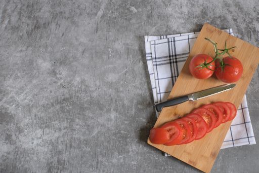 A top view of whole and sliced tomatoes on a wooden food board with a striped kitchen towel
