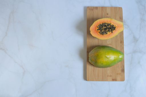 A high angle shot of fresh papaya on a wooden cutting board on a white surface