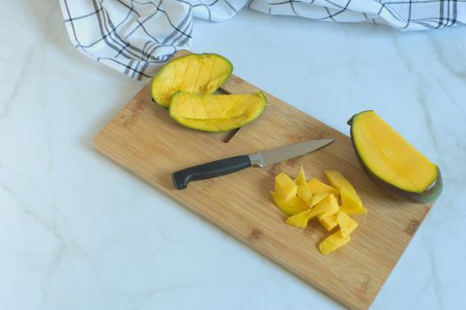 A high angle shot of fresh mango fruits on a wooden cutting board on a white surface
