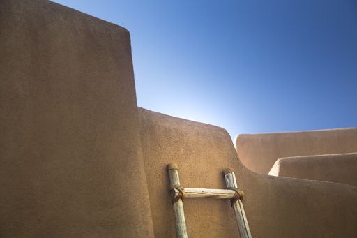A low angle shot of a wooden ladder leaning on a stone building under the bright sky