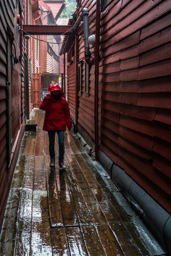 A vertical shot of a person in a raincoat walking in a narrow alley in the Bergen old town, Norway
