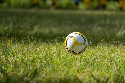 A close-up of a soccer ball on a grassy field with blurred players in the background.