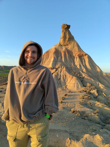 A young man in a hoodie in front of a unique rock formation during sunset in Bardenas Reales, Spain