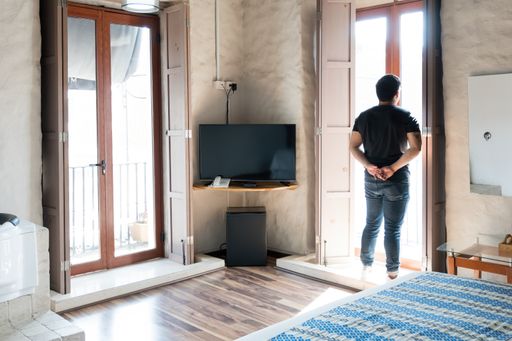 A view of a Hispanic man wearing a black t-shirt and a pair of jeans looking out of the window