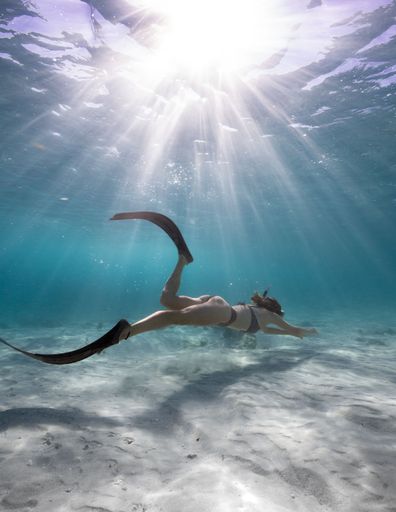 Underwater photo of a snorkeler swimming in clear blue ocean water with sunlight filtering through the surface.