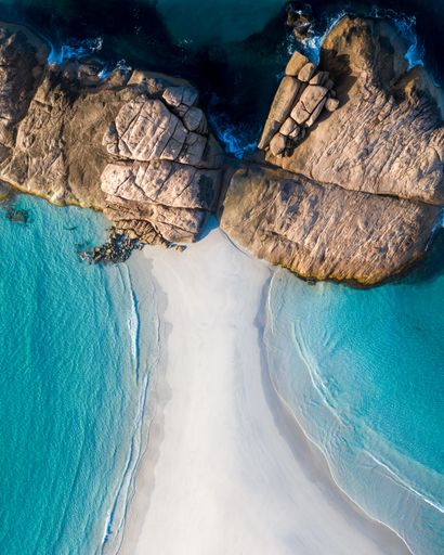 Aerial view of a pristine beach with clear turquoise waters and rocky formations, showcasing the natural beauty of the coastline.
