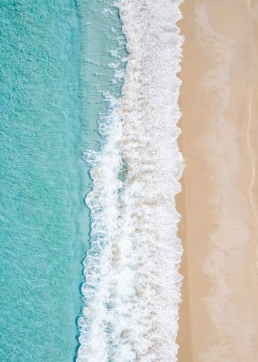 Aerial view of a sandy beach with turquoise waves crashing on the shore