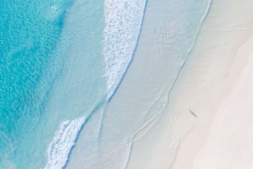 Aerial view of a pristine beach with turquoise waters and gentle waves, featuring a lone person walking on the shore.