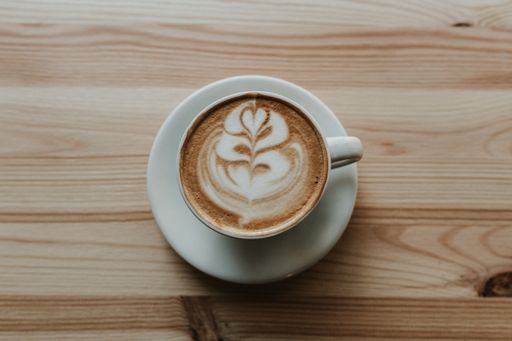 A closeup shot of coffee with latte art in white ceramic teacup on a wooden table