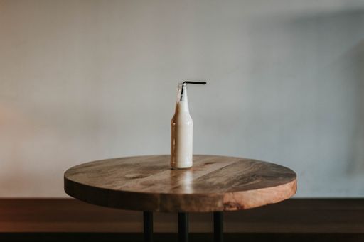 A shot of a glass bottle with a black straw filled with a beverage on a brown wooden table