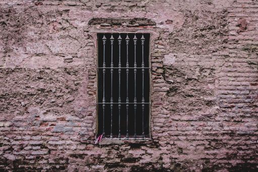 A closeup shot of an old weathered brick wall with a spiked metal window covering it