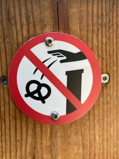 A vertical shot of a sign forbidding throwing pretzel on the wall