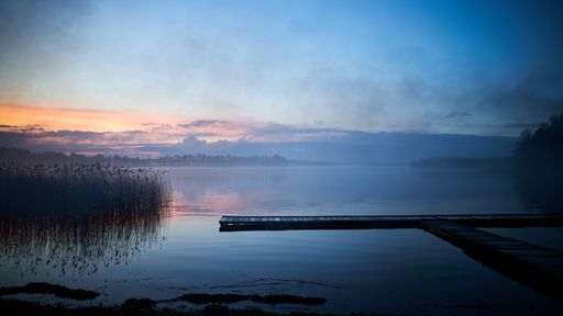 A serene lakeside view during twilight with a wooden pier extending over the calm water