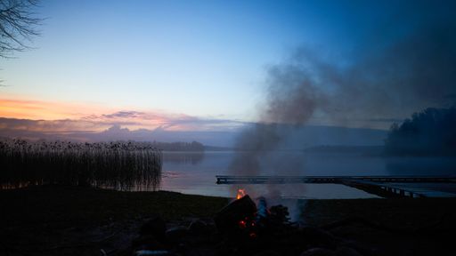 A serene lakeside view at dusk with a small campfire and a wooden pier extending into the water