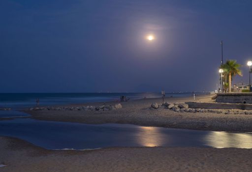 Scenic view of a beach at night with a full moon and street lights illuminating the promenade