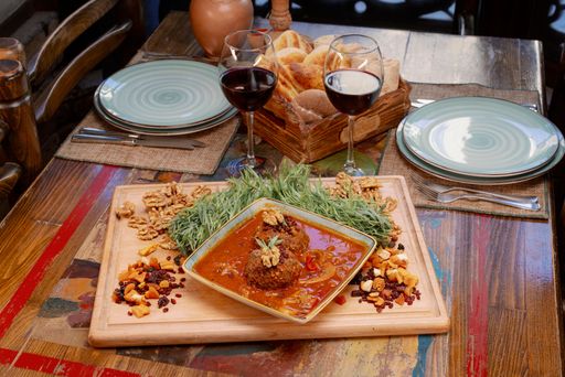 A rustic dining setup featuring a delicious meal of meatballs in sauce, walnuts, dried fruits, and two glasses of red wine on a wooden table.