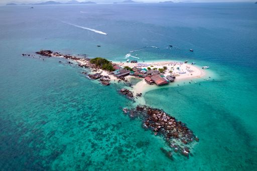 Aerial view of a Khai Nok island with clear turquoise waters, beach umbrellas, and boats in Thailand