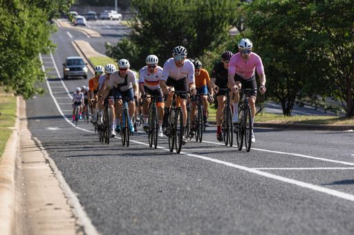 A group of cyclists on the road during the event of Pedal Around Austin in Texas on a sunny day with car in the background and trees on sides