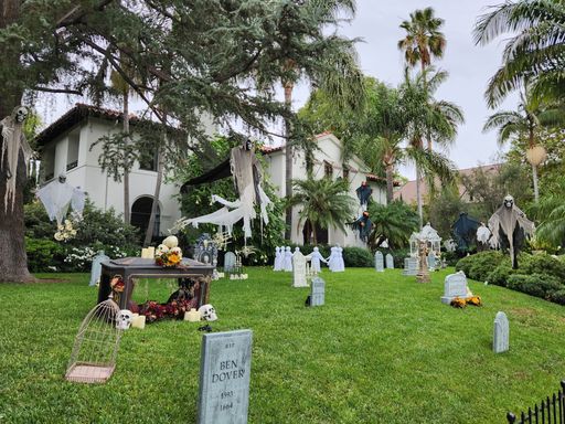 A house in Los Angeles decorated with Halloween props and tombstones in the front yard, surrounded by lush greenery and palm trees.