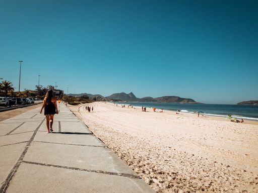 A back view of a female walking on the paved path along the sandy beach