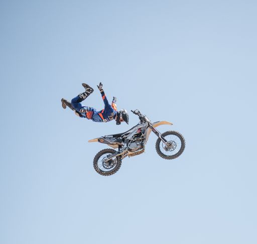 A motocross rider performs an aerial stunt against a clear blue sky.