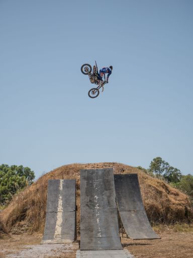 A motocross rider performing a high jump trick over ramps under a clear blue sky