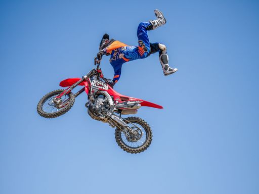 A motocross rider performing an aerial stunt on a red dirt bike against a clear blue sky.