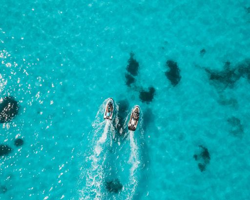 An aerial view of two jet skis on clear blue ocean water creating white trails