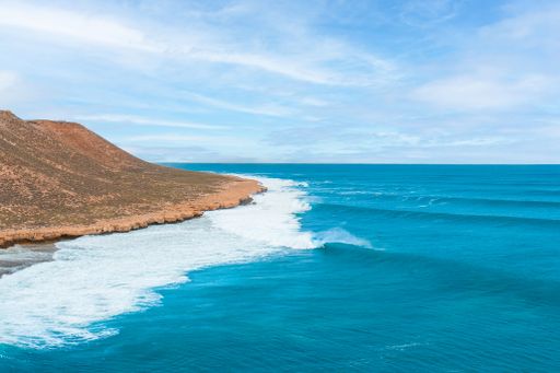 A stunning coastal landscape with clear blue ocean waves crashing against rocky cliffs under a bright sky.
