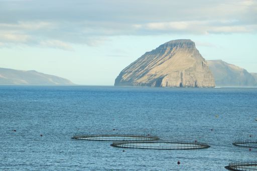 Scenic view of a mountain island with fish farming cages in the ocean under a cloudy sky