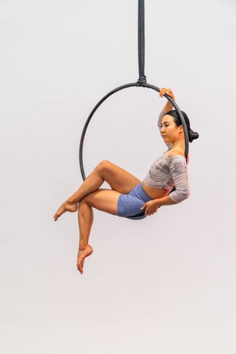 A woman gracefully performs aerial hoop gymnastics against a white background.