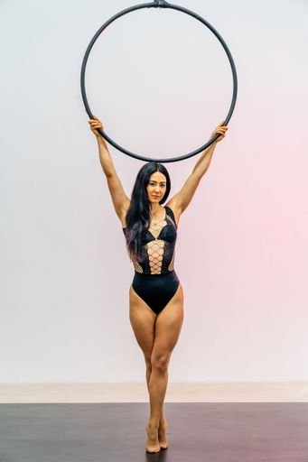 A young woman poses with an aerial hoop in a studio wearing a black leotard